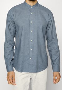 Camicia a maniche lunghe con bottoni in tessuto blu chiaro con una trama texture, dotata di colletto alla mandarina e bottoni bianchi.