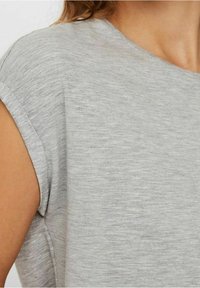 Primo piano di una persona che indossa una maglietta grigia chiaro a maniche corte con colletto girocollo e sottile texture orizzontale.