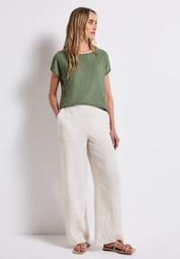 Grön texturerad kortärmad topp som matchas med löst sittande vita linbyxor. Sandaler med tunna remmar fulländar outfiten.