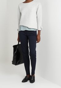 Světlé šedé zkrácené svetr s texturovanou tkaninou přes světle modrou vrstvu halenky, spárované s námořnickými slim-fit kalhotami a černými mokasíny. Černá kabelka.