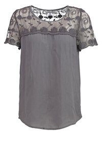 Blouse grise à manches courtes avec empiècement et manches en dentelle florale transparente, encolure ronde et corps en tissu doux et froissé.