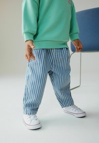 Mintgrüner Pullover, blau-weiß gestreifte Hose und weiße Sneakers mit roten Akzenten. Glatte Texturen, lässige Passform und entspannter Stil.