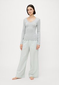 Haut gris clair à manches longues avec un col en V, associé à un pantalon à jambe large rayé vert menthe. Les deux sont fabriqués dans un tissu doux.