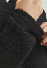 Schwarzer Pullover mit einem strukturierten, gerippten Muster und einem dicken Bündchen. Der Stoff wirkt weich mit einer leicht flauschigen Oberfläche.