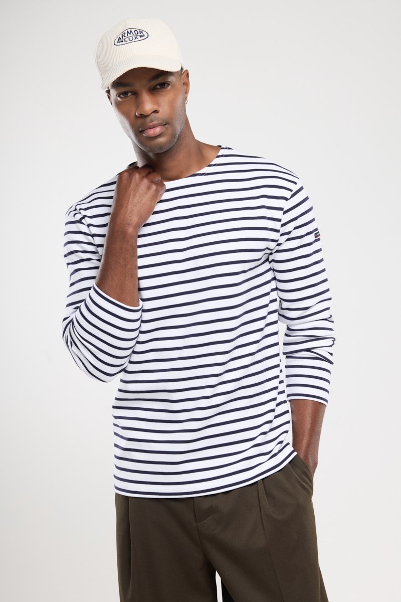 Weißes Langarmshirt mit marineblauen Streifen, runder Halsauschnitt und aufgekrempelten Ärmeln, kombiniert mit einer beigen Kappe mit einem marineblauen Logo-Patch.