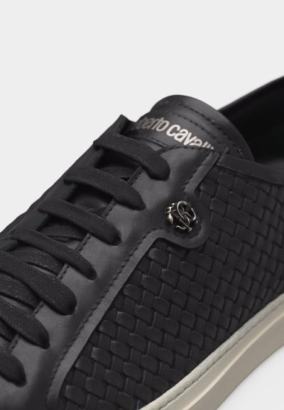 Baskets en cuir noir avec panneaux latéraux tissés, lacets noirs, logo de marque argenté près des œillets et semelle en caoutchouc blanche.