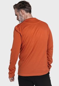 Langärmliges Shirt aus orangefarbenem Stoff mit glatter Textur und rundem Ausschnitt. Die Rückansicht zeigt Nähdetails und taillierte Ärmel.