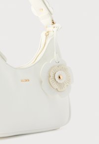 Sac à main synthétique blanc avec fermeture éclair dorée, orné d'un embellissement floral et de ferrures dorées. Surface texturée ; design incurvé.