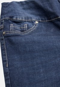 Mörkblå denimjeans med en framficka med sömnadsdetaljer och en metallknapp, som har en slät textur och en subtil blekning.