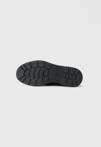 Suela de zapato de goma negra con un patrón de relieve texturizado, que incluye ranuras y acentos elevados para tracción y estabilidad. Marca Geox visible.