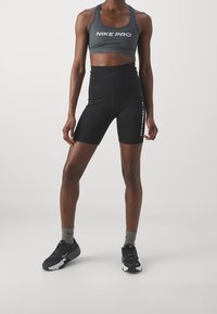 Czarny stanik sportowy Nike Pro z logo, czarne high-waisted spodenki, szare skarpetki sportowe oraz czarne sneakersy z białymi akcentami.