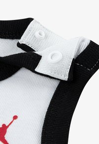 Body per neonato bianco e nero con chiusura a scatto, caratterizzato da un tessuto bianco liscio e una grafica rossa di un giocatore di basket.