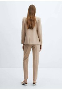 Costume taillé beige clair avec un blazer structuré et un pantalon droit. Le blazer a une fente simple et deux boutons ; le tissu semble lisse.