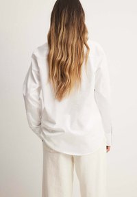 Witte lange mouwen shirt met een relaxte pasvorm, voorzien van een geknoopte manchette en een gebogen zoom, gecombineerd met gestructureerde beige wijde broek.