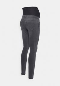 Jeans de maternidad en gris oscuro, con una cinturilla elástica negra alta, corte slim y dos bolsillos traseros con costuras visibles.