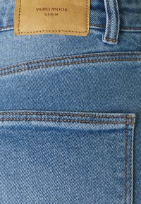 Primer plano de un bolsillo de jeans de mezclilla azul claro con costuras naranjas y una etiqueta de cuero que dice "Vero Moda Denim."