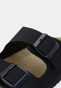 Μαύρο σανδάλι με δύο ρυθμιζόμενες αγκράφες, ματ υφή, μαλακό πέλμα και ανοιχτή σχεδίαση στο δάχτυλο. Εσωτερικό σε ανοιχτό καφέ χρώμα που δημιουργεί αντίθεση με το εξωτερικό.