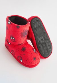 Röda fleece-inneskor med ett spindelnät-design, mjuk textur och en svart gummisula med mönstrat grepp för bättre fäste.