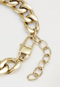 Bracelet en métal doré avec de grands maillons entrelacés, un fermoir et une chaîne d'extension avec un petit maillon ovale.