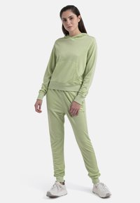 Conjunto de sudadera y pantalones jogger de color verde claro con una textura suave, que cuenta con un bolsillo delantero, puños acanalados y un corte holgado. Combinado con zapatillas blancas.