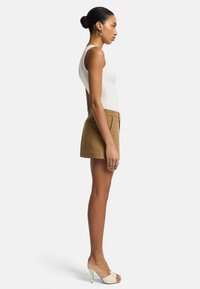 Tan shorts met een aansluitend ontwerp, zijzakken en een gedefinieerde tailleband, gecombineerd met een witte mouwloze top en beige hoge hakken.