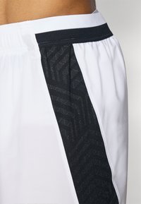 Weiße Sportshorts mit einem schwarzen gemusterten Einsatz und einem elastischen Bund mit Mesh-Details, die eine Kombination aus Texturen und Designs hervorheben.