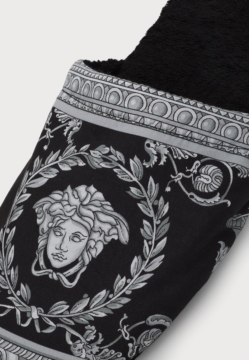 Black slipper with gray Medusa head design framed by laurel wreath and decorative border, lined with black soft fabric inside.