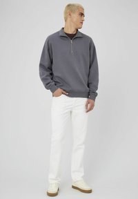 Sweatshirt zippé gris avec un col montant, associé à un jean blanc et des baskets crème. Texture lisse, coupe décontractée et design minimaliste.