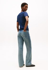 Navy blue t-shirt paired with light blue flared jeans, prominently featuring back pockets and raw hem detail. Black flat shoes.
