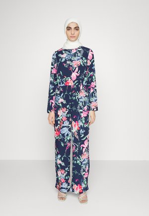 Macaquinho floral com um fundo azul-marinho e flores vibrantes em rosa, verde e azul. Manga longa e design fluido. Acessórios em hijab branco.