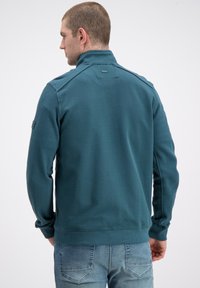 Sweter na zamek w kolorze morskim, wykonany z teksturowanej tkaniny, z wysokim kołnierzem, ściągaczami przy mankietach i subtelnym logo na szyi.