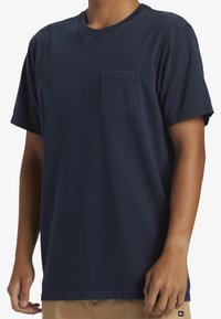 Mörkblå bomulls-T-shirt med rund hals, korta ärmar och en bröstficka på vänster sida. Har en avslappnad passform och enkla sömdetaljer.