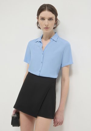 Light blue short-sleeve button-up shirt paired with a black wrap-style mini skirt. The outfit features smooth textures and simple designs.