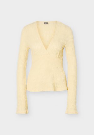 Pale yellow long-sleeve wrap top with textured fabric and deep V-neckline, fitted waist, and slightly flared hem.