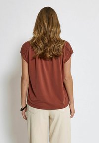 Top marrone a maniche corte con leggera arricciatura alle spalle, realizzato in tessuto leggero, abbinato a pantaloni color crema; texture liscia.