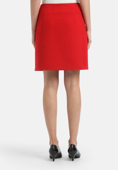 Mini gonna rossa in tessuto testurizzato, con una vita liscia e una silhouette dritta. Tacchi neri a punta completano l'outfit.