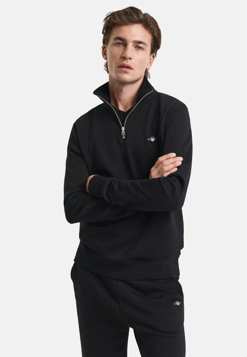 Black sweatshirt with a quarter-zip collar and ribbed cuffs. Features a small logo on the left chest and a soft, smooth texture.