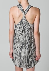Vestido sin mangas, de longitud hasta la rodilla, en beige con un patrón negro que imita el mármol; presenta un diseño de espalda retorcida y una tela suave y texturizada.