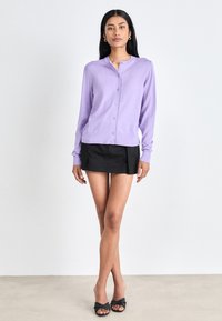 Lavendel, långärmad cardigan med rund halsringning och framknappning; mjuk textur kombinerad med en svart minikjol. Enkel och åtsittande design.