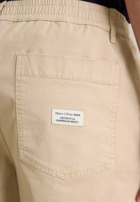 Beige cotton shorts featuring an elastic waistband and a back pocket with a stitched label from Marc O'Polo. Smooth texture, minimalist design.