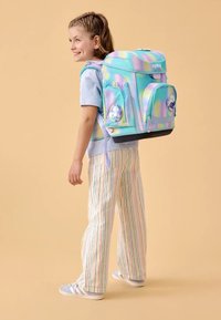 Sac à dos aux couleurs pastel iridescentes avec des motifs de bulles, deux poches avant, des bretelles rembourrées et une base noire solide. Porté par un enfant.