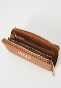 Portafoglio in pelle marrone con hardware dorato, chiusura con zip, molteplici compartimenti e logo impressa. L'interno presenta una fodera stampata.
