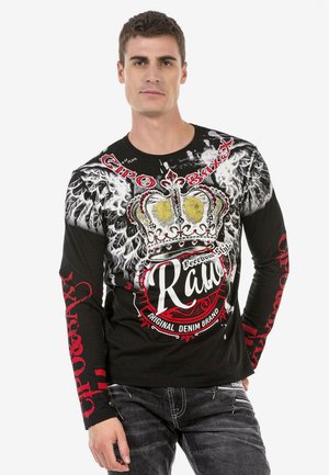 Schwarzes Langarmshirt mit einem auffälligen grafischen Kronendesign, verziert mit weißen Federn und roten Akzenten. Hergestellt aus Baumwolle mit bedrucktem Text und Mustern.