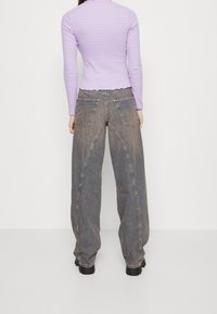 Długorękawowa bluzka w jasnofioletowo-różowe paski, zestawiona z szerokimi spodniami dżinsowymi z przetarciami, posiadającymi kieszenie i unikalne przeszycia.