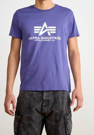 Fioletowy bawełniany t-shirt z białym nadrukiem z napisem "ALPHA INDUSTRIES" i motywem gwiazdy na przodzie.