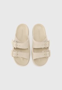 Beige sandaler med to justerbare stropper, laget av myk semsket skinn og gummi. Har en konturert fotbed og subtil merking på stroppene.