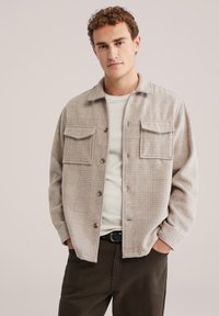 Beige ruudulise flanellaaniga jope, millel on kaks rinna-taskut, nööbid ja veidi laiem l�õige. Kandmisel heledama T-särgi peal.