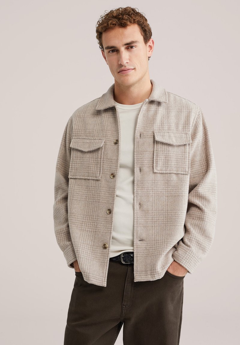 Beige ruudulise flanellaaniga jope, millel on kaks rinna-taskut, nööbid ja veidi laiem lõige. Kandmisel heledama T-särgi peal.