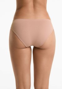 Beige naadloze bikini onderkant met een lage taille, gladde textuur en eenvoudig ontwerp, dat een minimalistische esthetiek benadrukt.