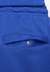 Blå textil med en bakficka som stängs med knapp. Mjuk textur, elastisk midjeband och en avslappnad passform.